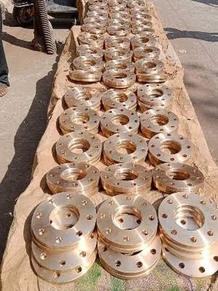 Row of machined bronze flanges laid out on a workshop table